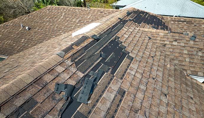 Damaged and missing asphalt roof shingles exposing roof underlayment
