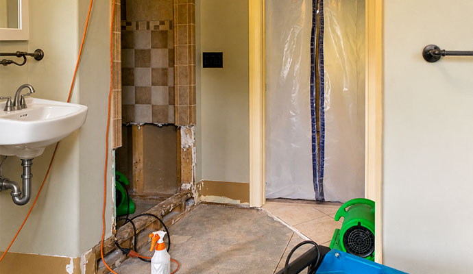 Bathroom undergoing water damage structural drying with air movers and containment barrier