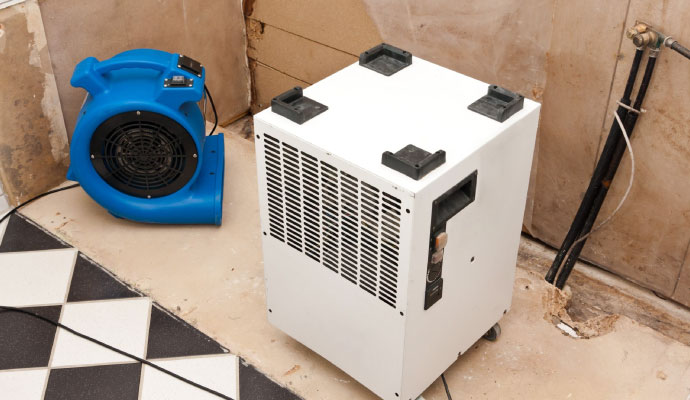 Commercial dehumidifier and blue air mover fan drying a room after a clogged drain overflow