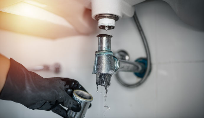 Gloved technician inspecting and cleaning a clogged sink drain pipe with dripping dirty water