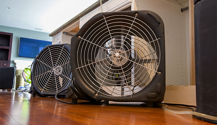 Two industrial drying fans placed on hardwood floor in front of kitchen cabinets