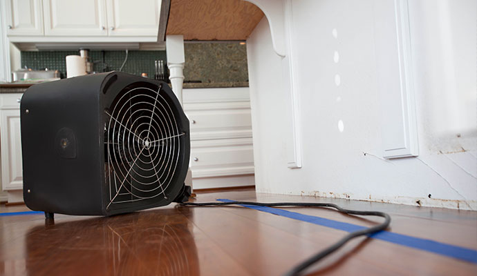 Industrial air mover drying fan blowing air along kitchen cabinets and hardwood floor after a drain overflow