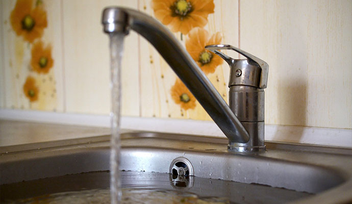 Running faucet filling a clogged kitchen sink with overflowing dirty water