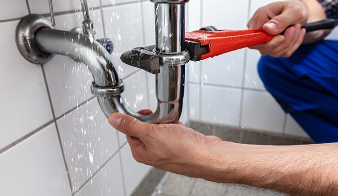 A plumber fixing a leaking pipe under a kitchen sink using a wrench