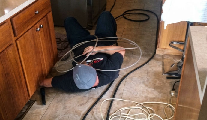 Restoration technician lying on kitchen floor inspecting hidden water damage beneath cabinets