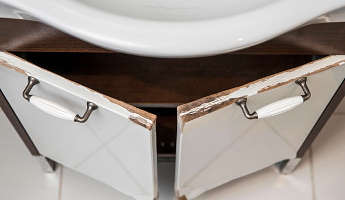 Water damaged and warped bathroom vanity cabinet doors beneath a sink